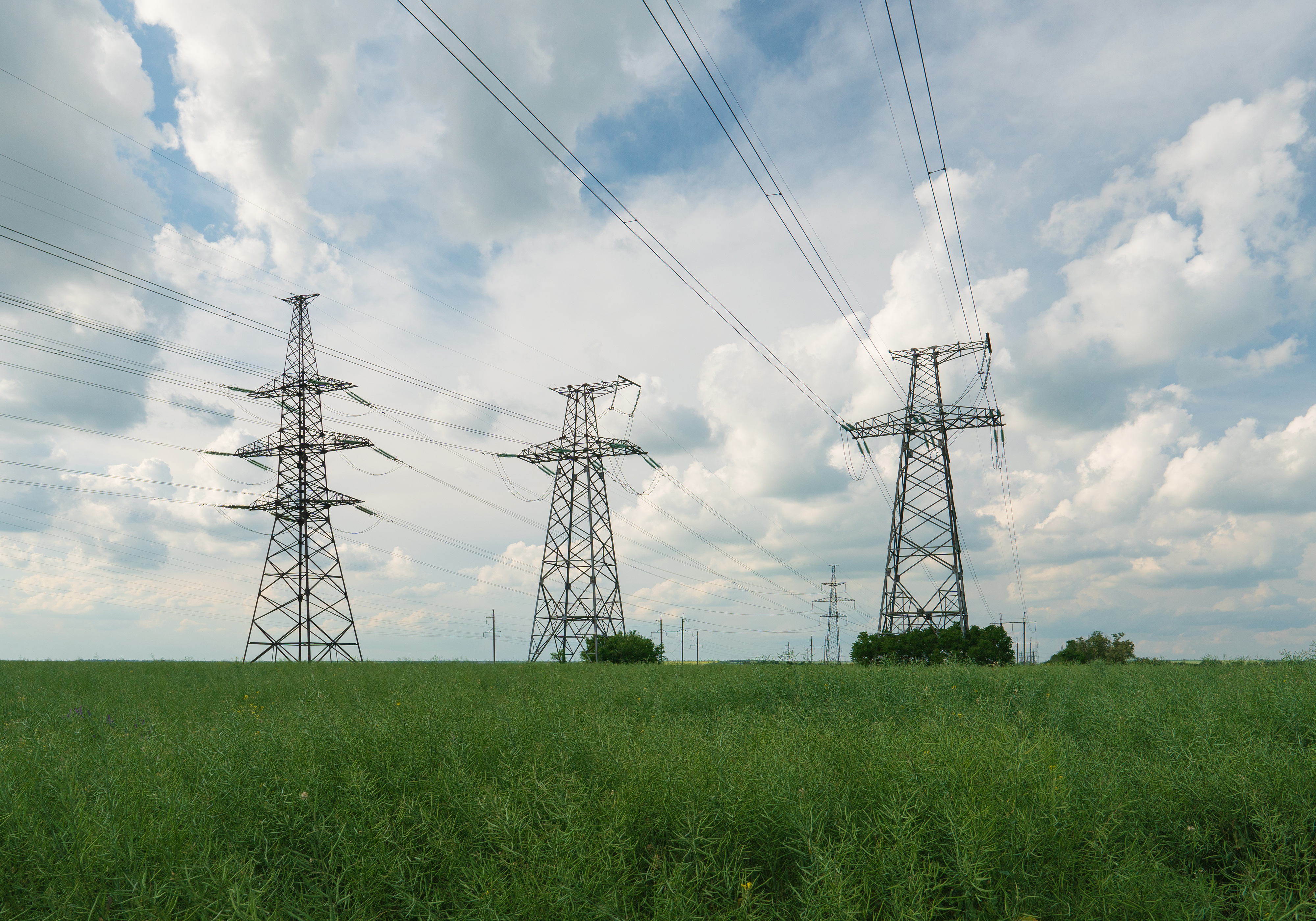 Three electricity tranmission towers in a grassy field with cloudy sky in the background