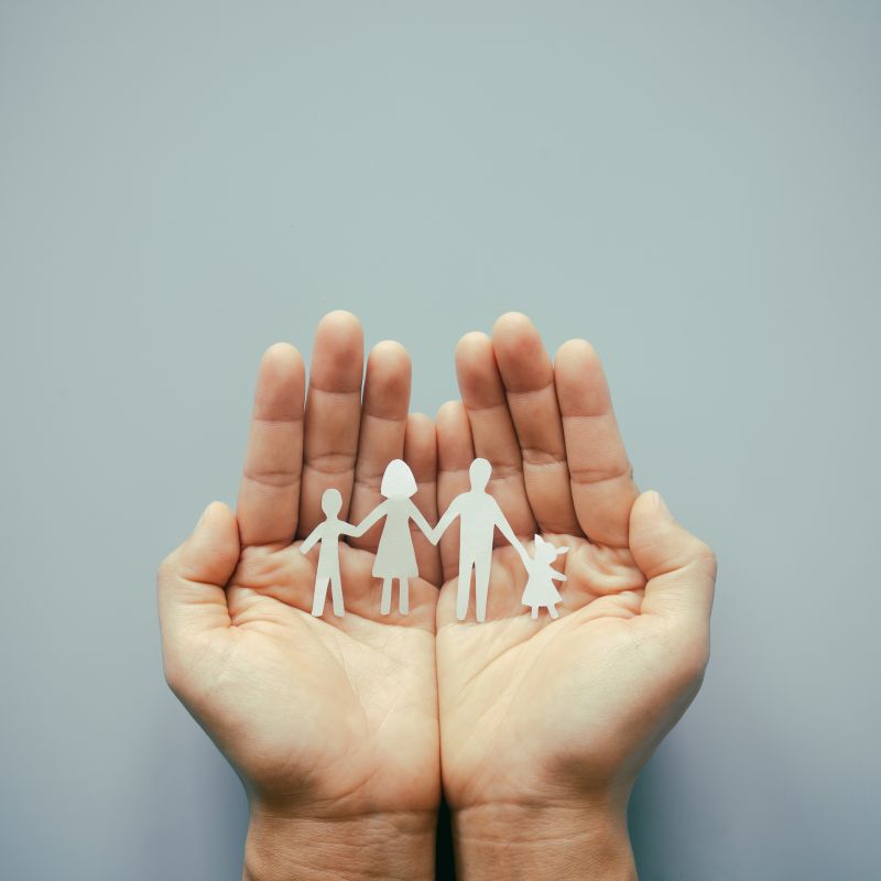 Two hands cupped together with paper cut outs of a family of four 