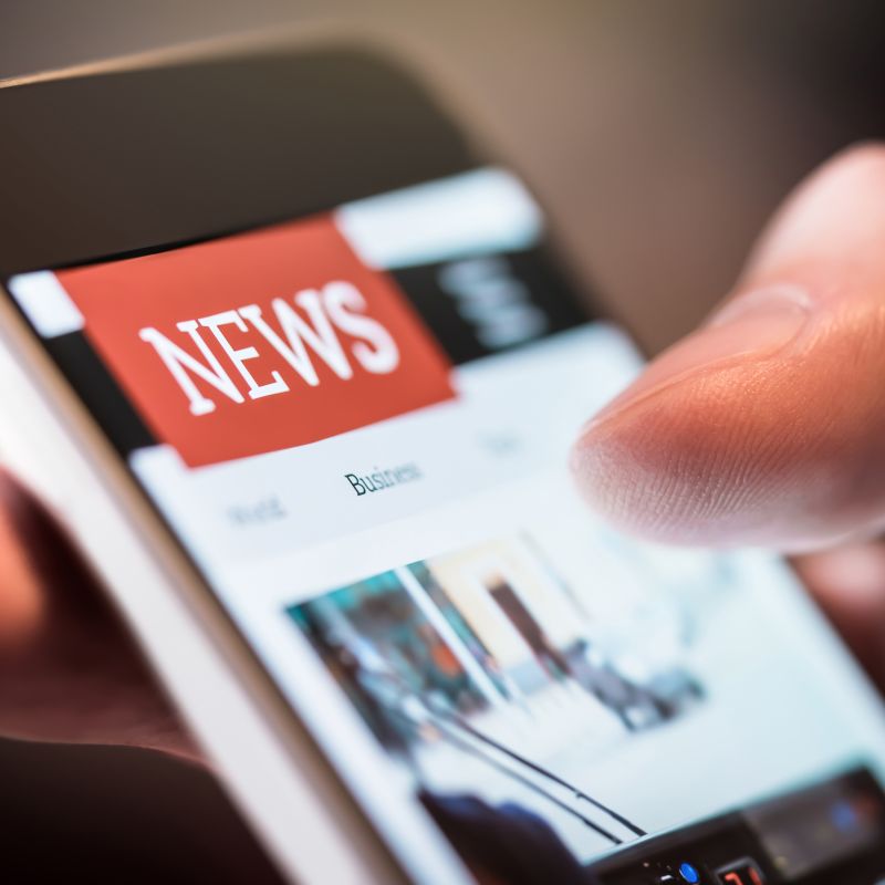 A hand holding a mobile phone showing the heading News