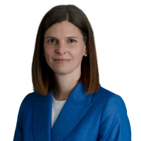 A corporate head shot of Kate Symons wearing a blue suit, smiling at the camera.