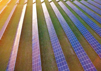 The sun setting over rows of solar panels in a solar farm that supplies electricity to the grid