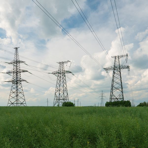 Three electricity tranmission towers in a grassy field with cloudy sky in the background